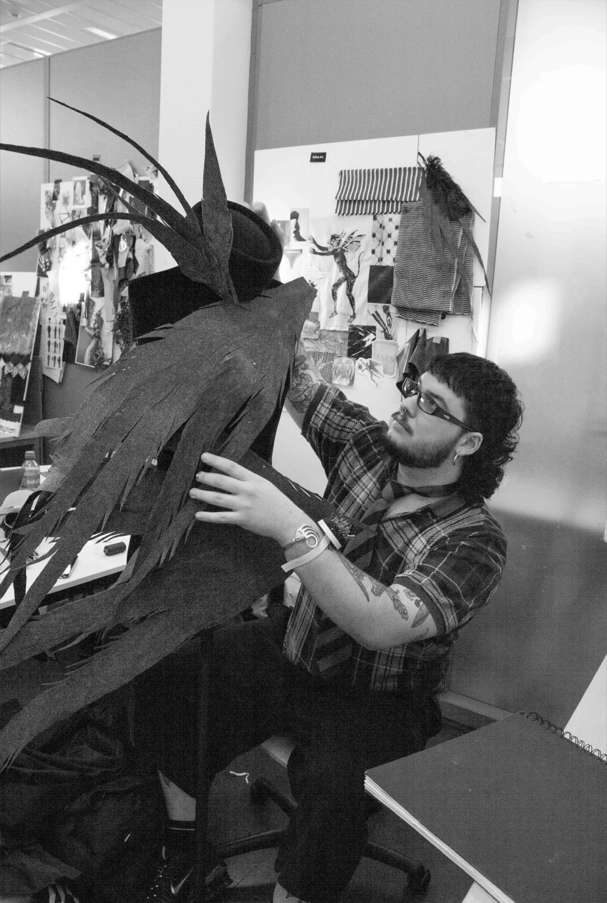 Storm Nijhuis wearing glasses while adjusting a sculptural Hellion garment in the studio.