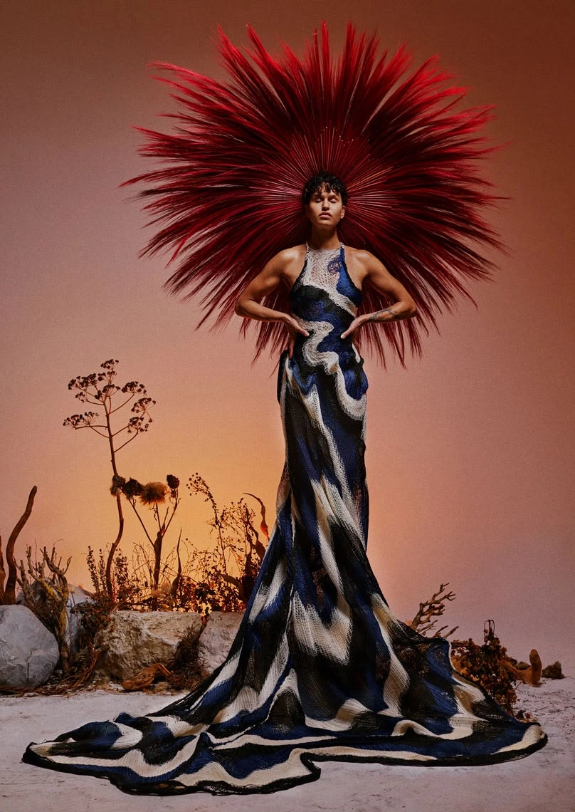 Maria Anouk standing in a flowing patterned dress and a large red headpiece for Binhe. Design assistance and product design by Storm Nijhuis for Zyanya Keizer.
