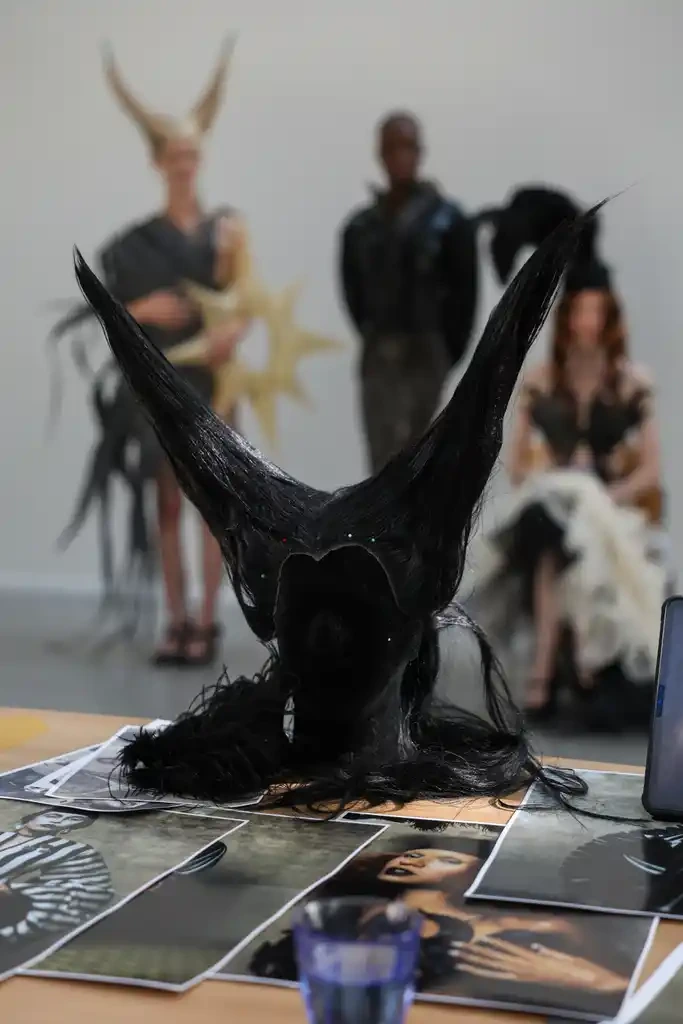 A sculptural Hellion headpiece on a table beside the collection research.