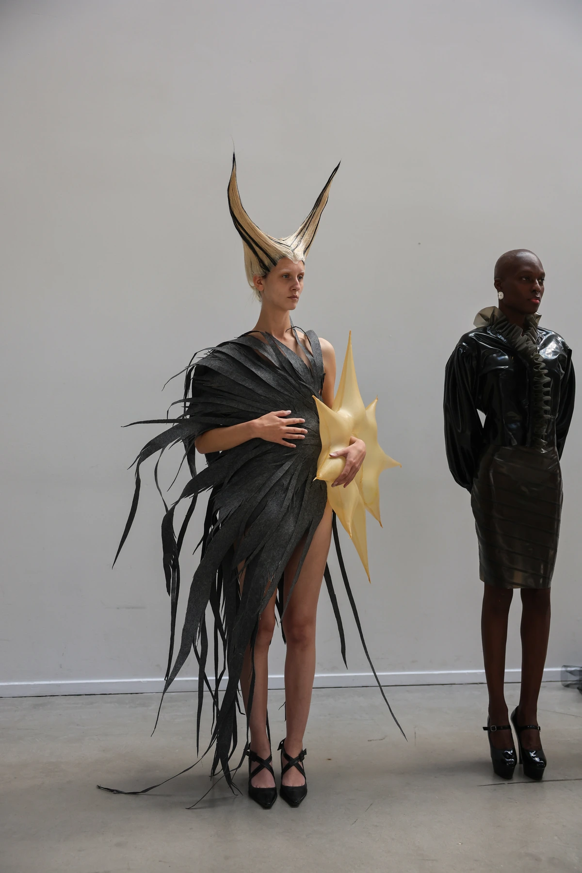 Two models wearing sculptural Hellion looks at a collection presentation.